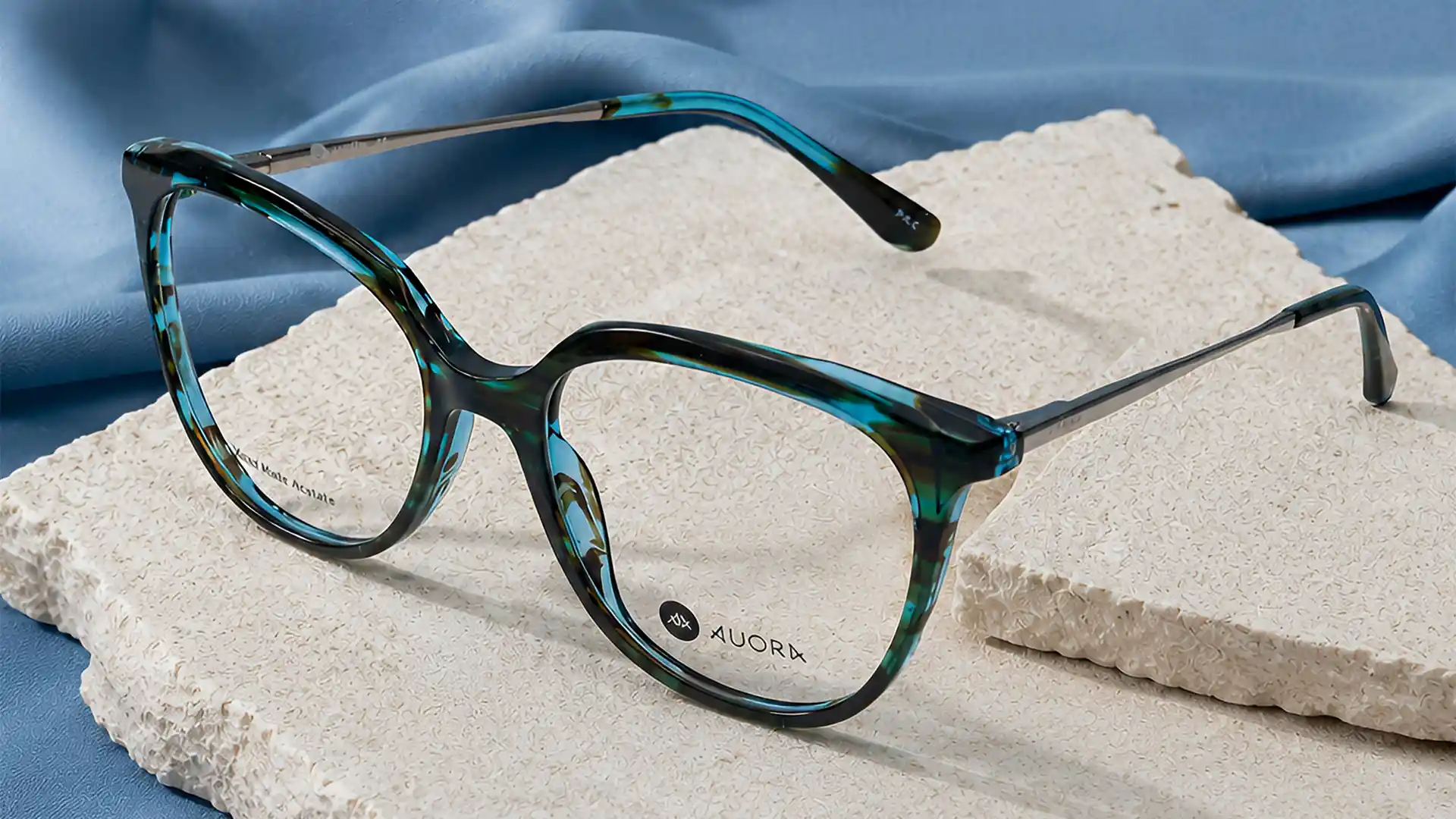 Auora Eyewear blue tortoiseshell optical frame on a textured stone surface.