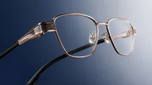 Auora Eyewear gold metal optical frame with black temples on a blue background.
