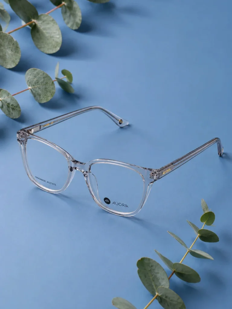 Auora Eyewear transparent optical frame on a blue background with eucalyptus leaves